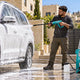 Man washing a foam-covered SUV in a driveway with an electric pressure washer