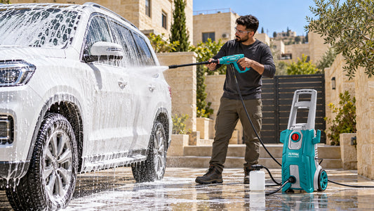 Man washing a foam-covered SUV in a driveway with an electric pressure washer